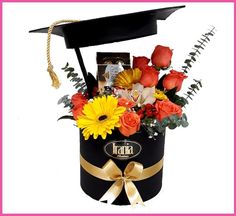 a graduation hat with flowers in it on top of a black box and gold ribbon