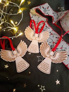 three wooden angel ornaments with red ribbon and lights in the background on a black table