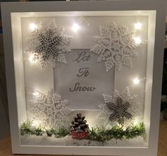 a lighted frame with snowflakes and pine cones in the center that says let it snow