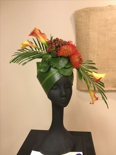 a black mannequin head with flowers and leaves on it's head, next to a lamp shade