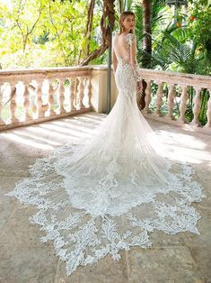 a woman in a wedding dress standing on a balcony with palm trees and greenery