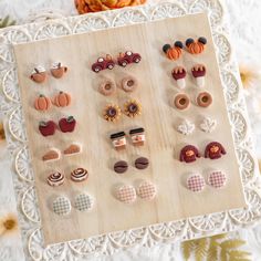 there are many different types of earrings on the table next to some pumpkins and flowers