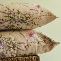 two pillows sitting on top of each other in front of a white wall with purple and pink flowers