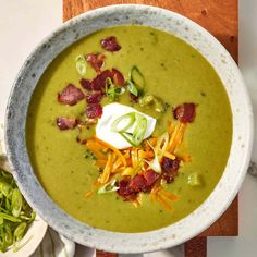 a bowl of soup with bacon, cheese and other toppings on the side next to a salad