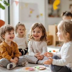 three children sitting on the floor laughing and playing with magnets in front of them