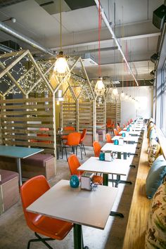 an empty restaurant with orange chairs and tables in the foreground, lights hanging from the ceiling