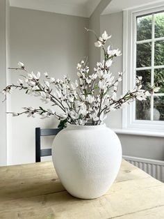 a white vase filled with flowers on top of a wooden table next to a window