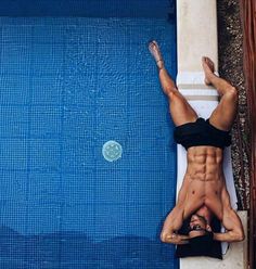 a man standing on his back in front of a swimming pool with no shirt on