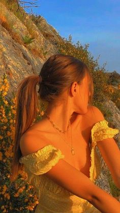 a woman in a yellow dress is sitting on a rock and looking at the ocean