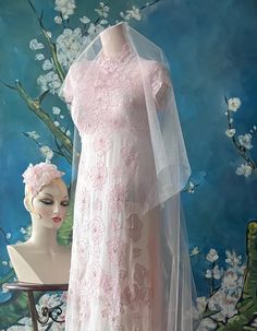 a mannequin wearing a pink dress and veil in front of a wall with flowers