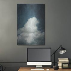 a desk with a computer, books and lamp in front of a painting on the wall