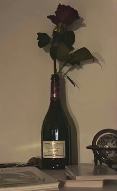 a wine bottle with a rose in it sitting on a table next to some books