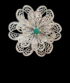 The delicately handcrafted traditional South American filigree sterling silver 975 brooch (from Mompox, Colombia) is adorned with a .5 carat Colombian round emerald in a five-prong setting.  The voluminous brooch has three layers of petals; each petal containing the stunning intricacies of filigree wire. Specifications: ~0.5ct Colombian Emerald ~Emerald shape: round ~Emerald setting: 5 prong ~Material: 975 Silver ~Brooch diameter:  1.75inches (45cm) ~Brooch weight: 21 grams  Questions? Please send us a message! Traditional Hallmarked Brooch For Formal Occasions, White Heirloom Brooch Jewelry, Flower Shaped Wedding Brooches Hallmarked, Ornate White Gold Brooches For Wedding, Heirloom White Brooch Jewelry, Elegant Ceremonial Filigree Brooches, Wedding Flower Brooches Hallmarked, Wedding Flower Brooch Hallmarked, Ornate White Gold Wedding Brooches