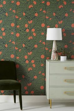 a green chair sitting next to a white dresser with a lamp on top of it