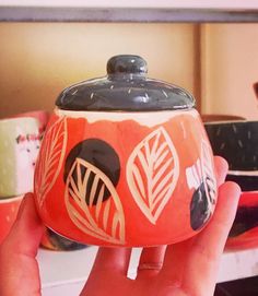 a hand holding a red and black container with designs on the lid in front of other bowls