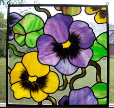 a close up of a stained glass window with flowers in the center and green grass behind it