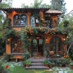 an orange house with lots of potted plants and flowers on the front porch, surrounded by greenery