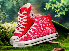 a pair of red converse sneakers sitting on top of green moss covered ground with white flowers in the background