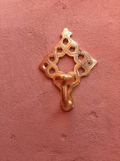 a gold door handle on the side of a pink wall with an intricate design in the middle