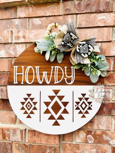 a wooden sign that says howdy hanging on a brick wall with flowers and greenery