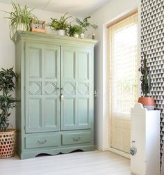 a green armoire sitting next to a window with potted plants on top of it