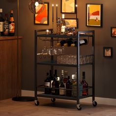 a bar cart with bottles and glasses on it in front of a wall filled with pictures