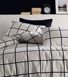 a bed with black and white checkered comforter, pillows and an alarm clock