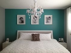 a white bed sitting under a chandelier in a bedroom next to pictures on the wall