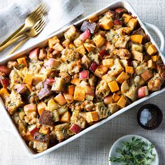 a casserole dish filled with stuffing next to a plate and silverware on a table