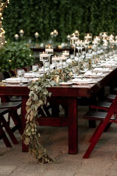 a long table with candles and greenery is set up for an outdoor dinner party