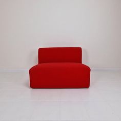 a red couch sitting on top of a white floor next to a wall in an empty room