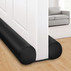 a black mat on the floor in front of a white door with a couch behind it