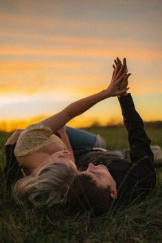 two people laying on the ground with their hands up in the air while the sun sets