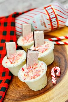 small cups filled with candy canes and marshmallows on top of a wooden plate