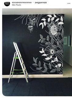 a black wall with white flowers painted on it and a ladder leaning against the wall