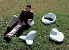 a man sitting on the ground next to three white chairs and one is holding a cell phone