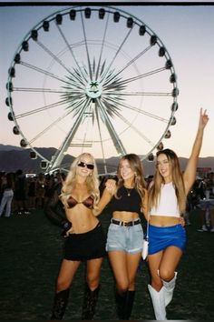 three beautiful women standing next to each other in front of a ferris wheel