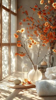 a vase filled with orange flowers sitting on top of a table next to towels and candles