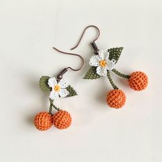 two crocheted oranges and white flowers are hanging from hooks on a white surface