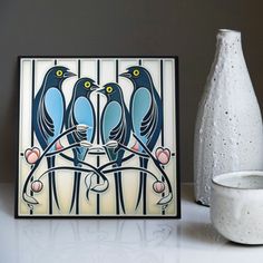 two blue birds sitting on top of a table next to a white vase and painting