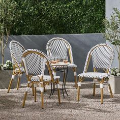 four chairs and a table in the middle of a graveled area with trees behind them