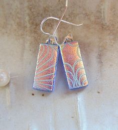 "The stones in these beautiful earrings measure approximately 13/16\" by less than 3/8\".  They are hung with sterling silver French wire hooks and hang approximately 1 1/4\".  The pattern on these earrings were sand blasted onto the glass, and then coated with dichroic.  When fired and left un-capped with clear, it leaves a beautiful satin and shiny textured dichroic service.  The base glass in these earrings is transparent blue with peach-gold colored dichroic on top.   Thank you for looking in my shop.  All of my pendants and earrings will arrive in a gift box.  I do my best to accurately photograph my work so you will be happy with your purchase. Dichroic Glass changes colors with different lighting and different angles, therefore making it difficult to photograph. You must see my dich Sterling Silver Blue French Hook Earrings, Blue Sterling Silver Earrings With French Hook, Nickel-free Long Drop Blue Earrings, Nickel Free Long Drop Blue Earrings, French Wire, Dichroic Glass, Earrings Blue, Glass Earrings, Earrings Dangle