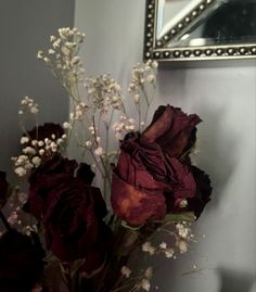 a vase filled with red roses next to a mirror