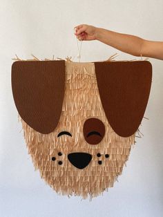 a person is holding up a dog made out of straw and paper strips, with the face of a dog on it's head