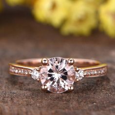 a close up view of a pink diamond ring on a wooden surface with flowers in the background