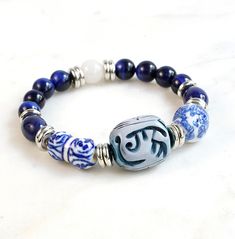 "Our new Vintage Collection bracelets are fashioned out of treasure hunted finds that have been reimagined, redesigned, and recreated into unique one of a kind keepsakes. We love bringing new life to these vintage treasures and making them new and timeless.  Carved focal bead is surrounded by ceramic blue and white beads, 8mm dark blue tiger eye and white moonstone. 7\" circumference, elastic fit" Handmade Symbolic Beaded Bangle Bracelets, Handmade Symbolic Beaded Bangle Bracelet, Vintage Adjustable Beaded Bracelets With 8mm Beads, Vintage Healing Bracelet Jewelry, Vintage Adjustable Beaded Bracelets For Gifts, Vintage Healing Bracelets, Vintage Healing Bracelet, Elegant Stretch Bracelet With Large Beads For Gift, Elegant Stretch Bracelet With Large Beads As Gift