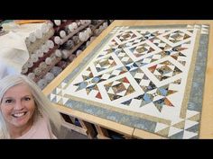 a woman standing in front of a table with many different quilts on top of it