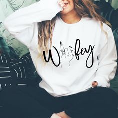 a woman sitting on top of a couch wearing a white sweatshirt with the word whineley printed on it