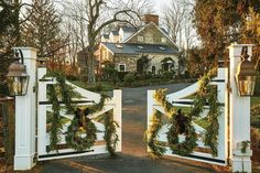 a white gate with christmas wreaths and lights on it in front of a house