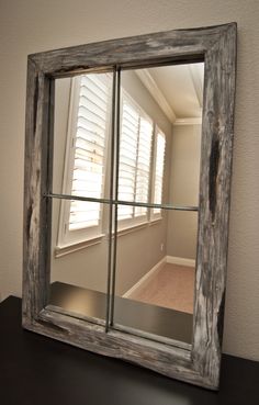 a mirror sitting on top of a wooden table next to a window with shutters